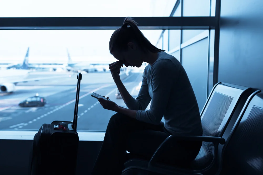 Woman at airport looking a smart phone with flight delayed